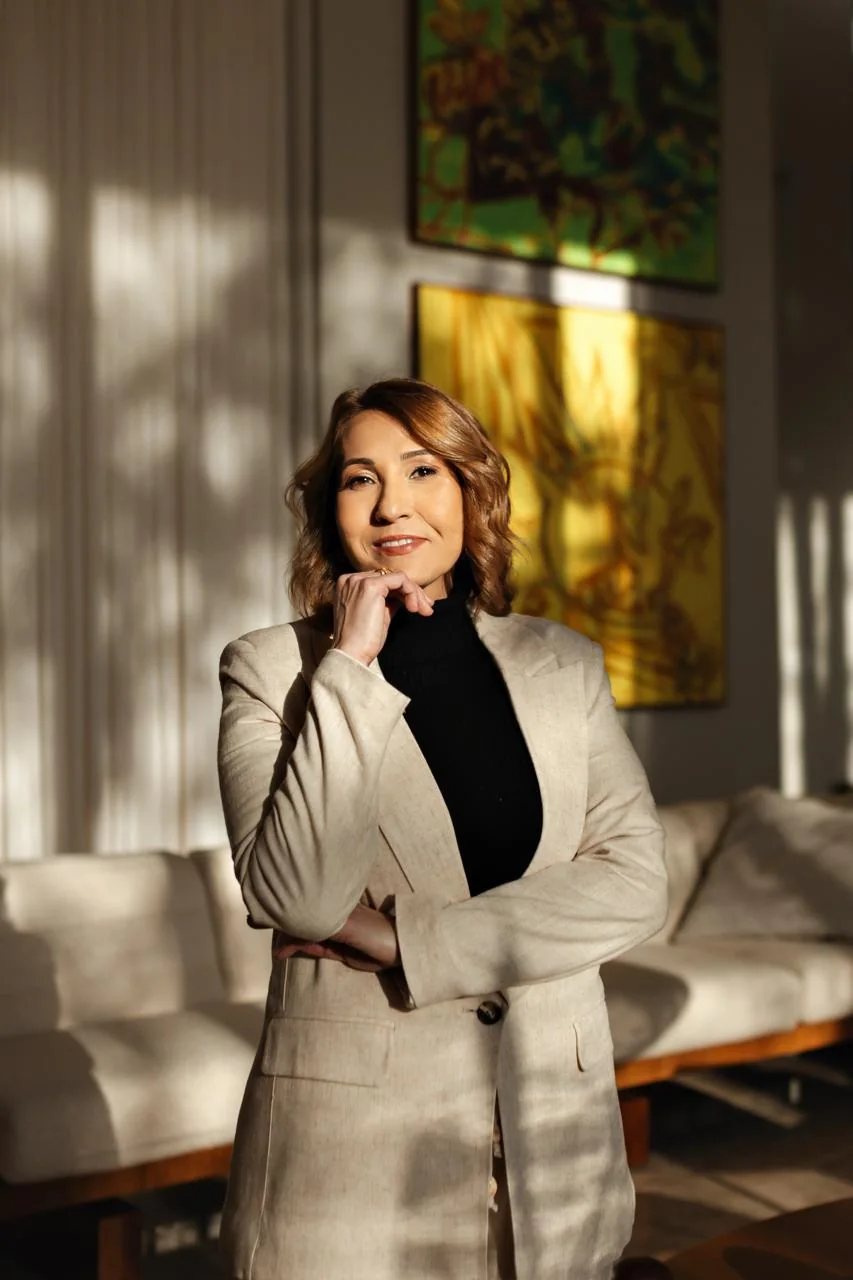 Lorenna Torres em pé na sala de atendimento, de conjunto claro, com a mão no queixo
